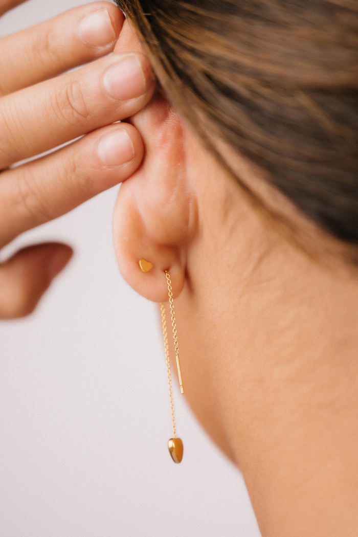 Close-up of a person wearing a gold threader earring with a hand adjusting it on a light background