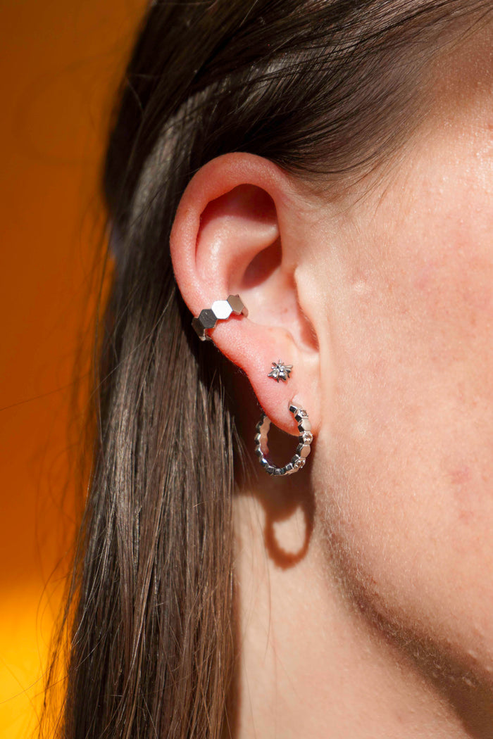 Close up of a model wearing a cuff earring made from stacked hexagon shapes. Hoop made from 18k gold-plated stainless steel.
