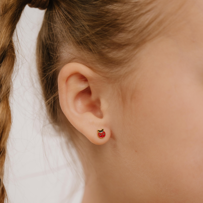 A close up of a ladybug shaped flat back stud with red enamel and gold-plated titanium metal.