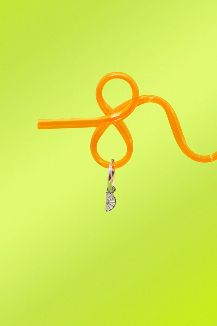 Orange straw with a silver 3D Lime wedge charm on a yellow-green background