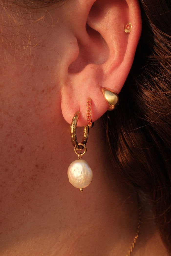 Close-up of an ear wearing gold hoop earrings with pearl drops.