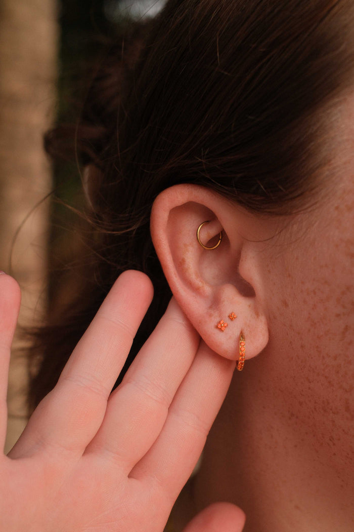 Close-up of an ear with two gold earrings, one being adjusted by a hand.