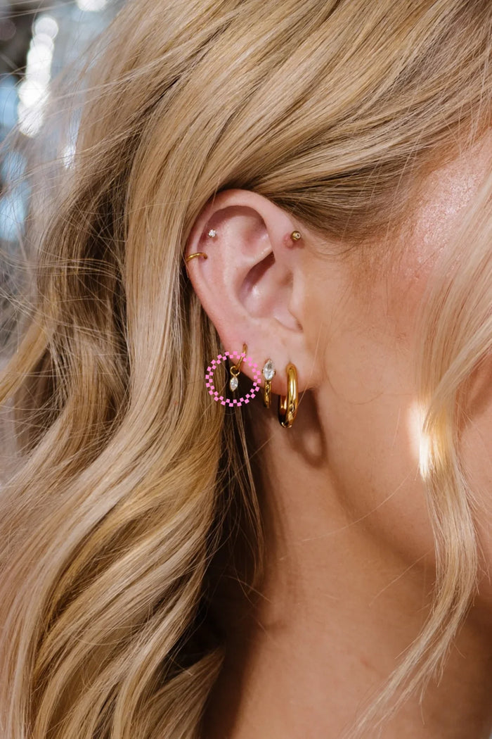 Close-up of a person wearing gold hoop earrings with pink and clear gemstones.