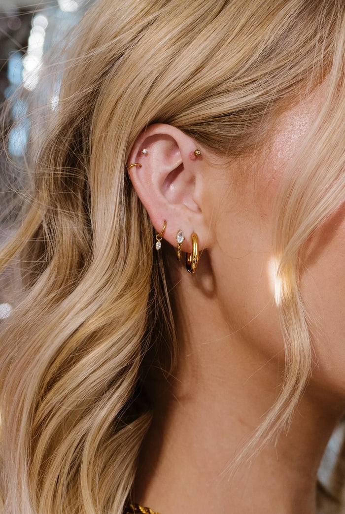 Close-up of an ear with gold hoop earrings and additional jewelry, blurred background