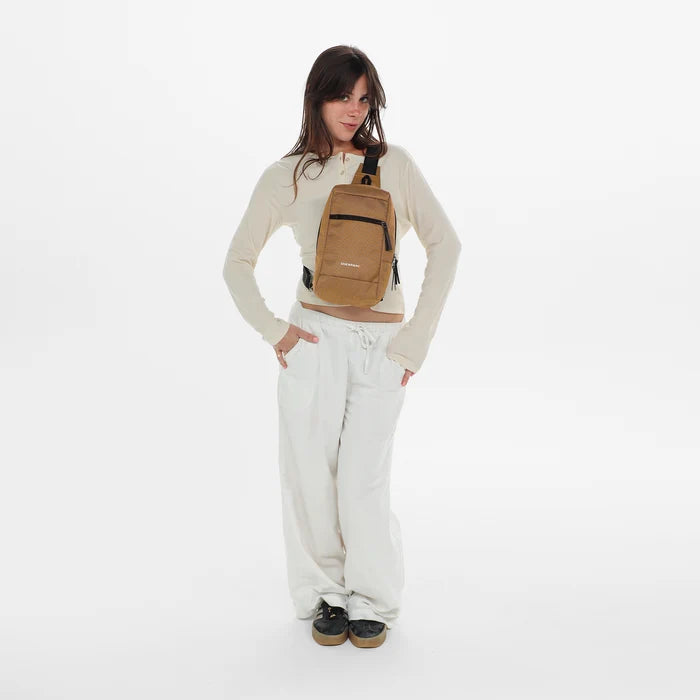 Woman wearing a Sherpani Metro Sand Anti-theft Reversible Sling on her front against white backdrop. #color_sand-tan