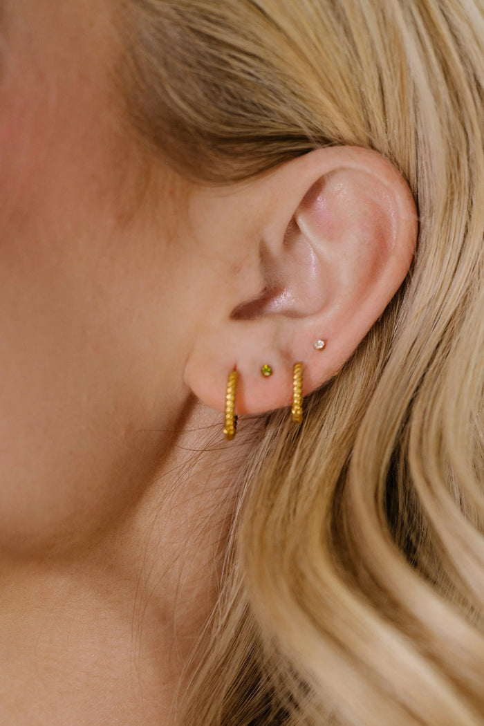 Close-up of a person with blonde hair, wearing two gold hoop earrings and two CZ stud earrings.