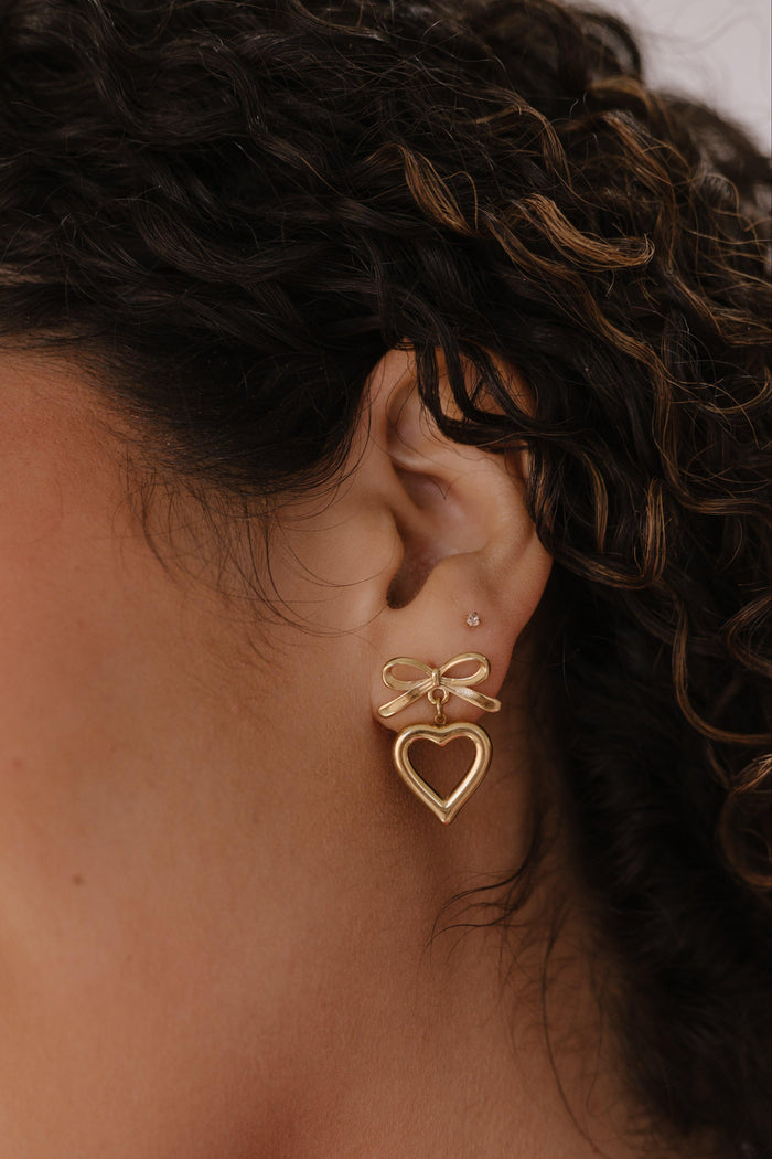 Close-up of a person wearing gold bow-shaped earrings with a neutral background
