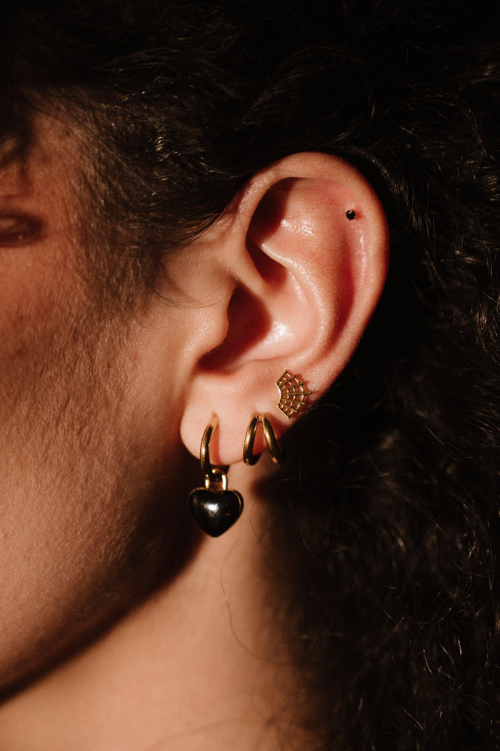 Close-up of an ear with gold and black earrings against a dark background