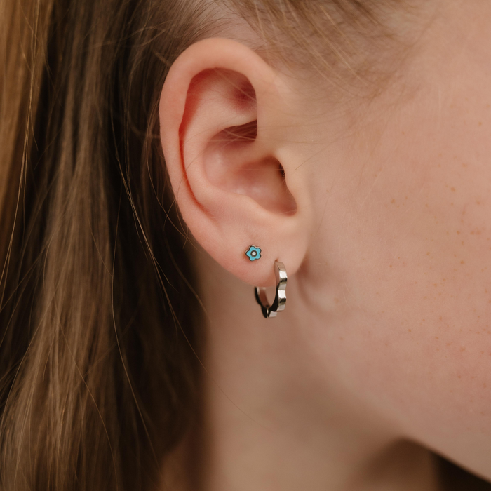 A close up of a daisy shaped flat back stud with blue enamel and titanium metal.