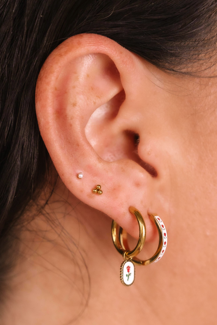 Close-up of an ear wearing gold hoop earrings with floral charms.
