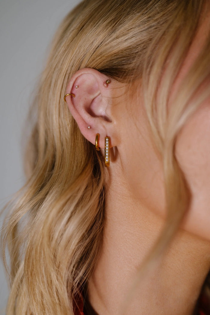 Close-up of a person's ear with gold hoop earrings against a neutral background