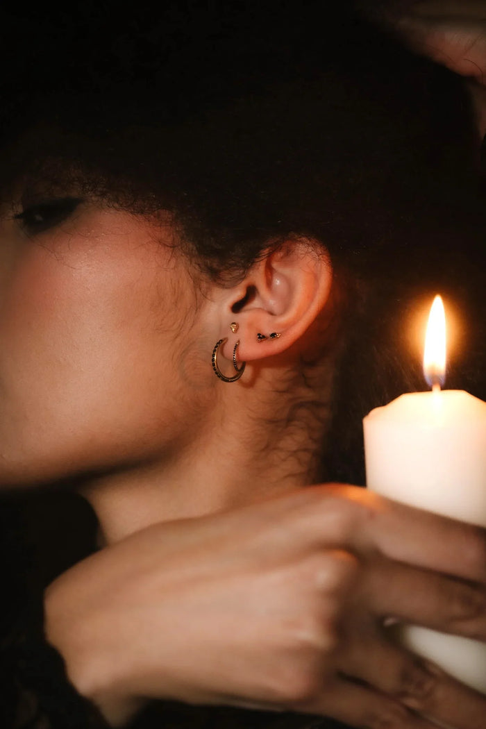 Close up photo of an ear wearing gold and black flat backs and hoops