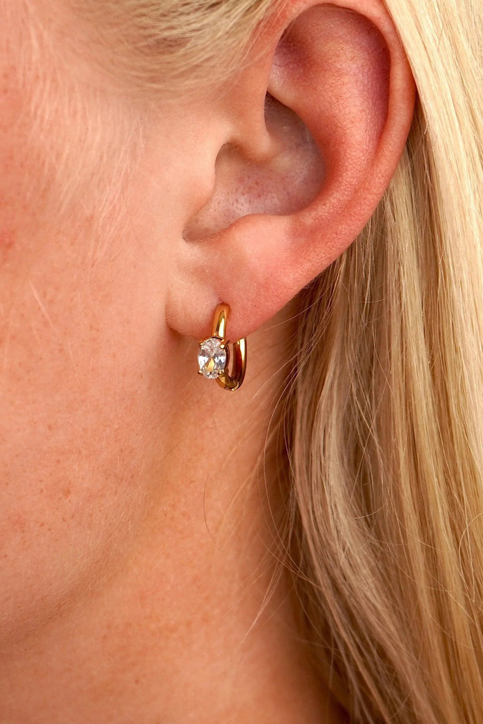Close-up of a person wearing a gold hoop earring with a clear gemstone.