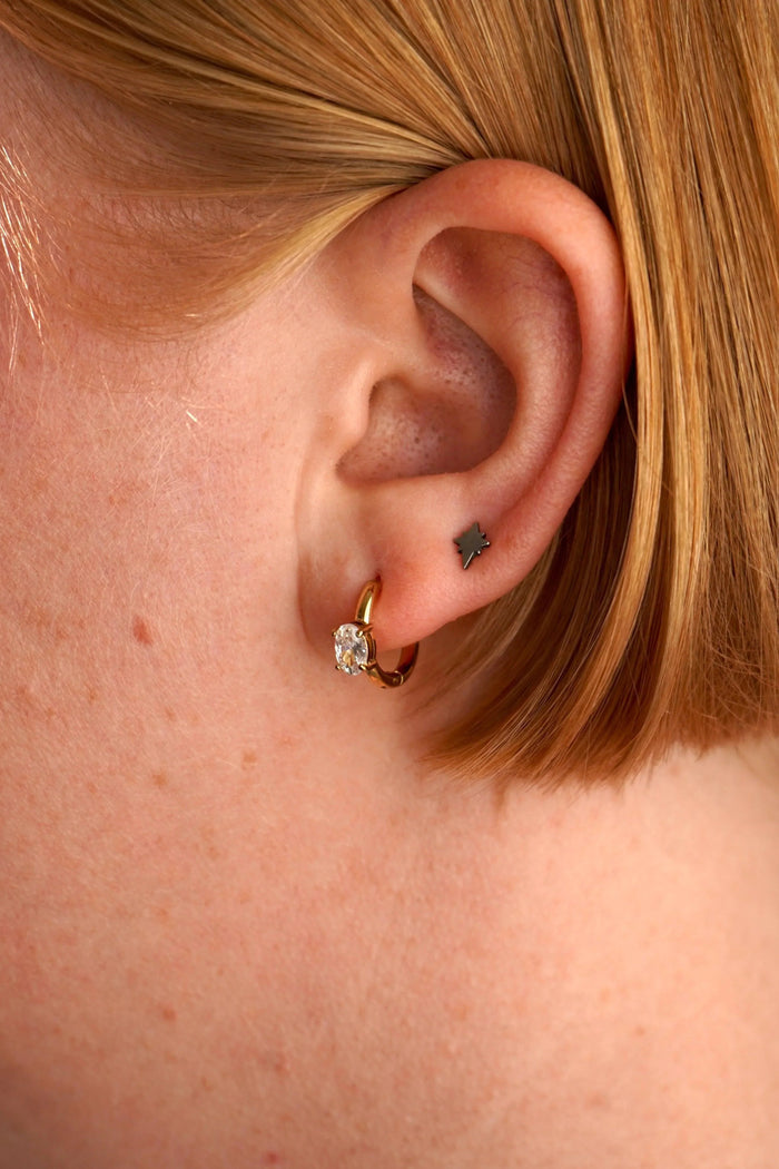 Close-up of an ear with a gold earring and black tattoo on the lobe.