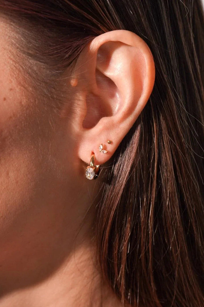 Close-up of an ear with gold earrings against a blurred background