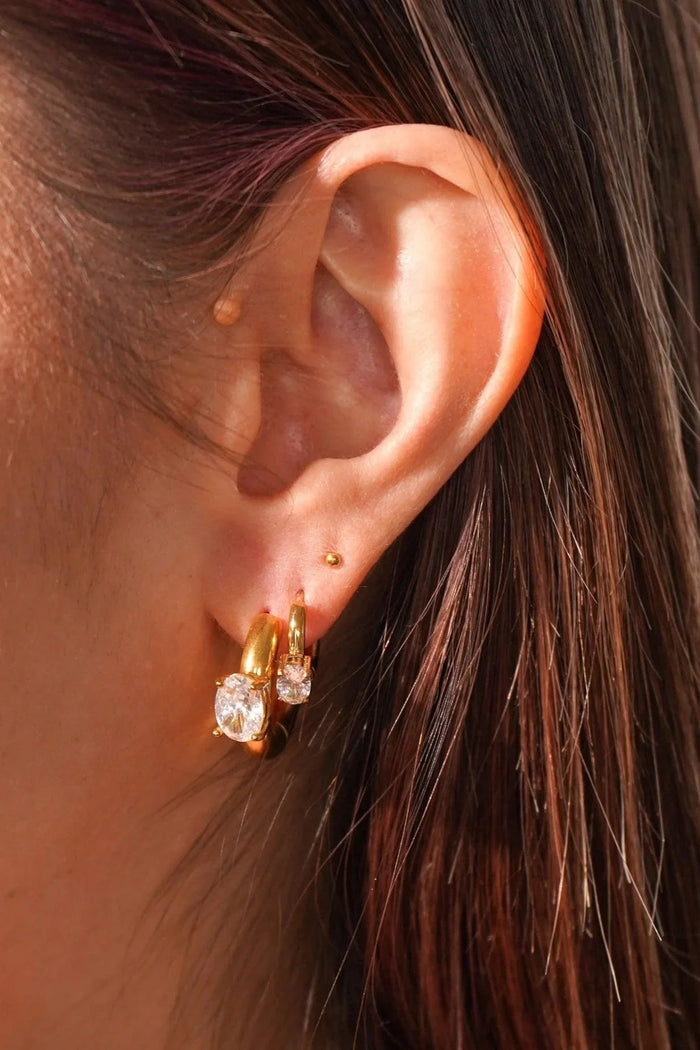 Close-up of an ear wearing gold and crystal earrings with a blurred background