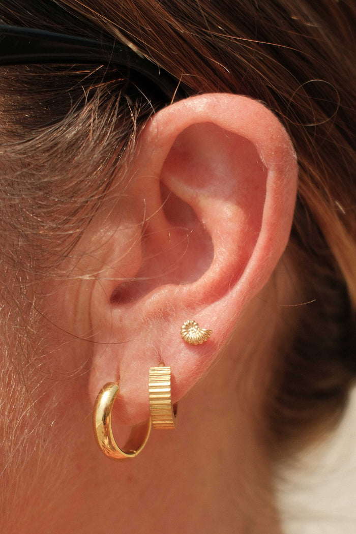 Close-up of an ear wearing gold hoop earrings with a blurred background