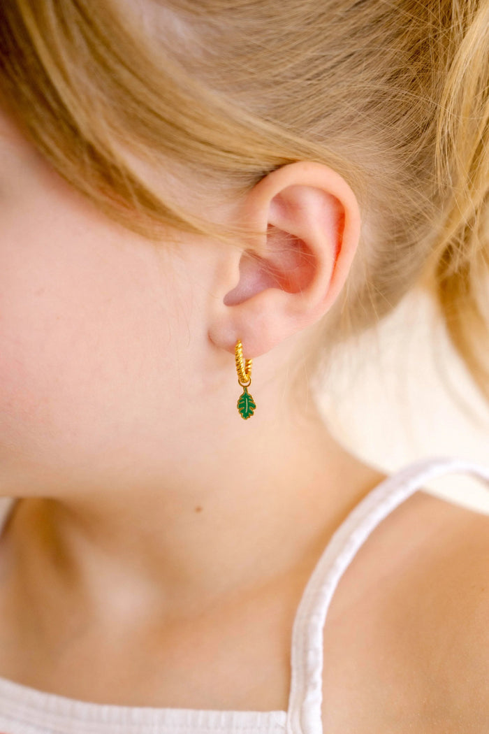 Close-up of a child wearing gold hoop earrings with green and gold oak leaf enamel hoop charm.