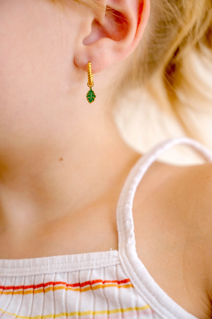 Close-up of a child wearing gold hoop earrings with green and gold oak leaf enamel hoop charm.