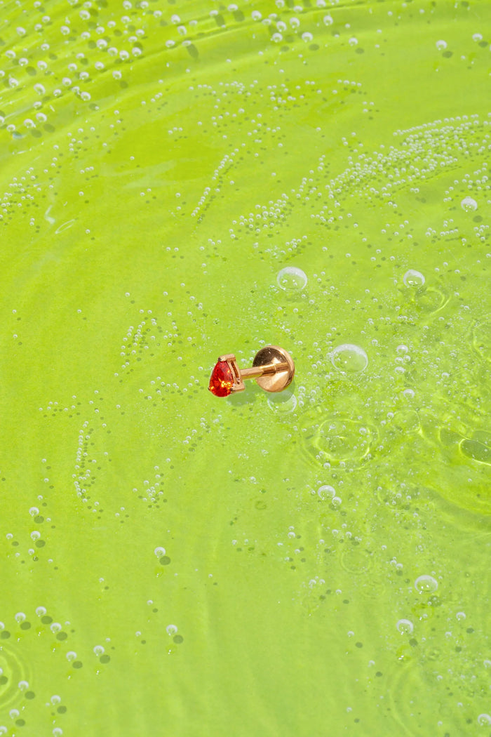 orange teardrop-shaped faceted gem flat back stud on a green textured surface with bubbles