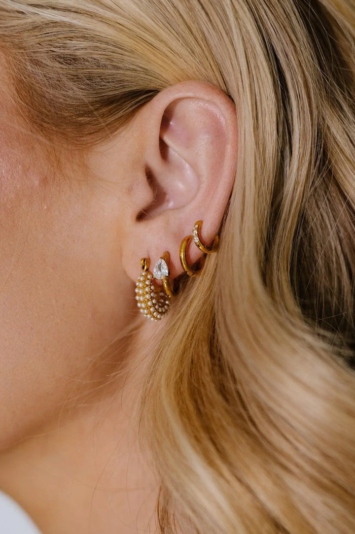 Close-up of a person wearing gold hoop earrings with a blurred background