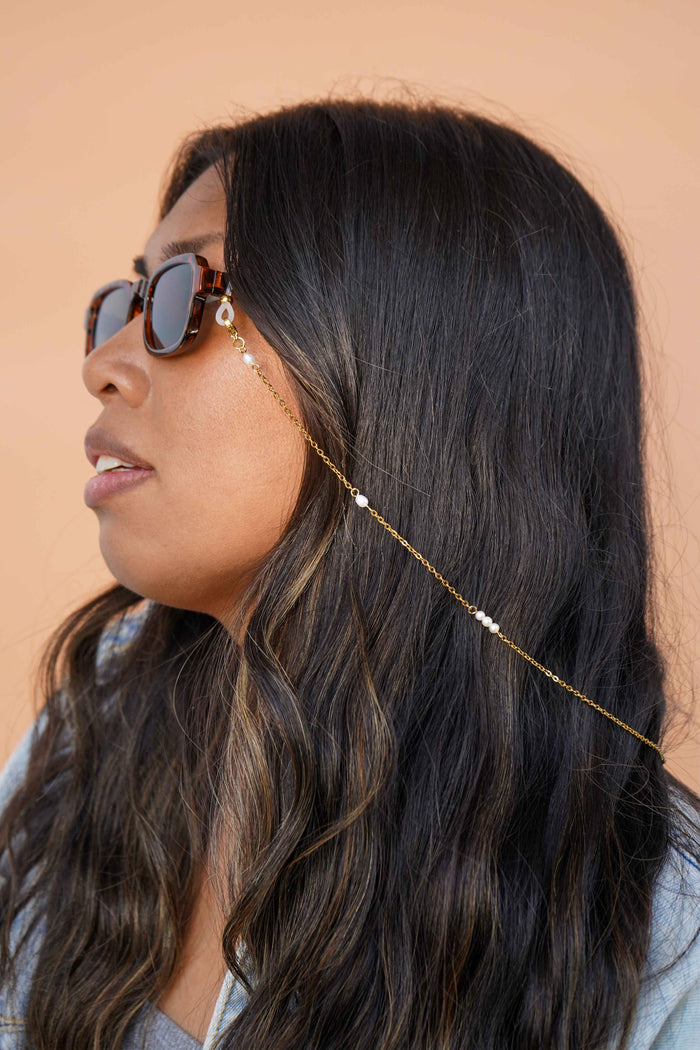 Woman wearing sunglasses with a gold glasses chain accessory against a beige background