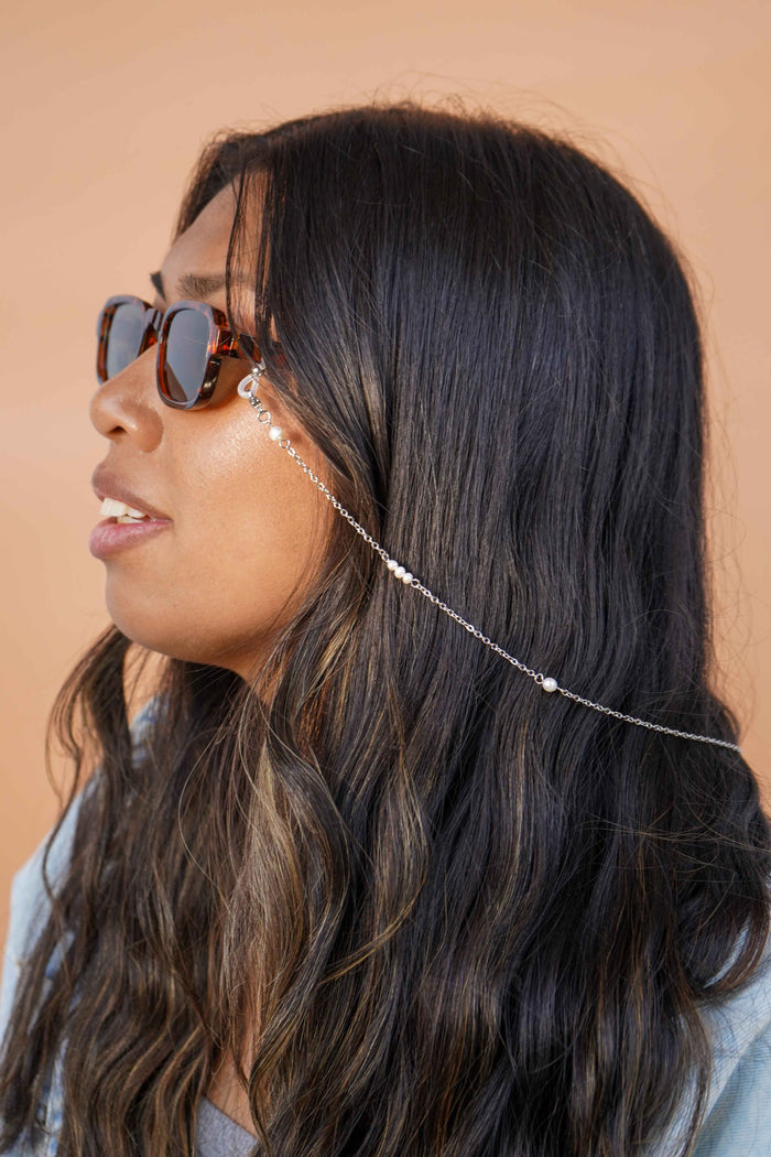 Woman wearing sunglasses with a silver glasses chain accessory against a beige background