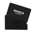 A Physical Gift Card with SHINOLA DETROIT in white lettering is partially inserted into a matching black sleeve embossed with the brand name, both displayed on a white background.