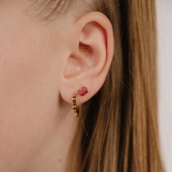 A close up of a butterfly shaped flat back stud earring with wings of pink enamel and gold-plated titanium metal.