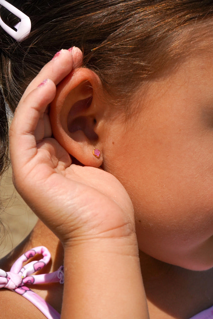 Close-up of a child's hand holding their ear, showcasing a purple shell earring.