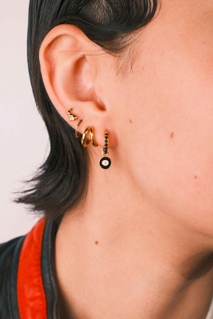 Close-up of an ear wearing gold and black earrings with a plain background