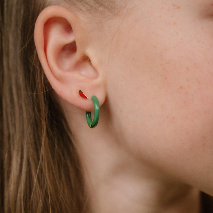 A close up of a chili pepper shaped flat back stud with red enamel and gold-plated titanium metal.