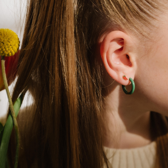 A close up of a chili pepper shaped flat back stud earring with red enamel and gold-plated titanium metal.