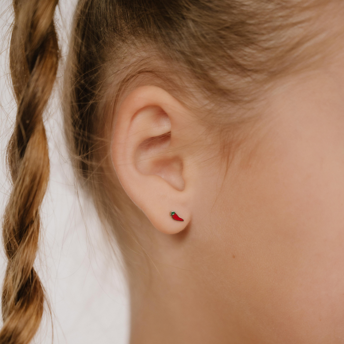 A close up of a chili pepper shaped flat back stud with red enamel and titanium metal.