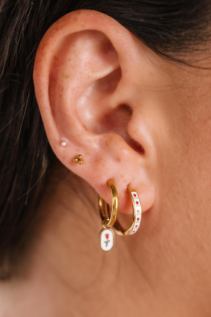 Close-up of an ear wearing gold hoop earrings with floral designs.