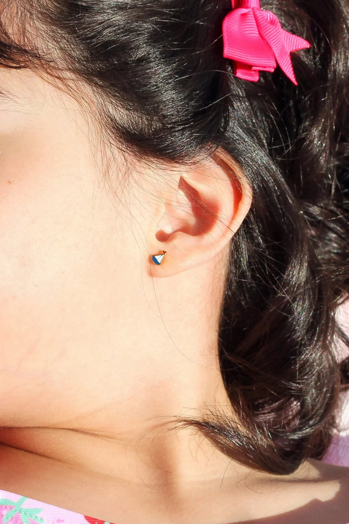 Girl with a pink bow in her hair wearing a sailboat earring and a pink shirt with strawberry pattern.