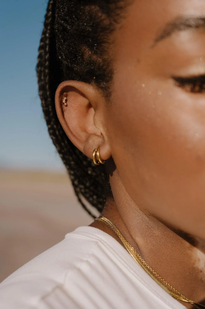 Close-up of a person wearing double gold hoop earrings with a blurred natural landscape in the background
