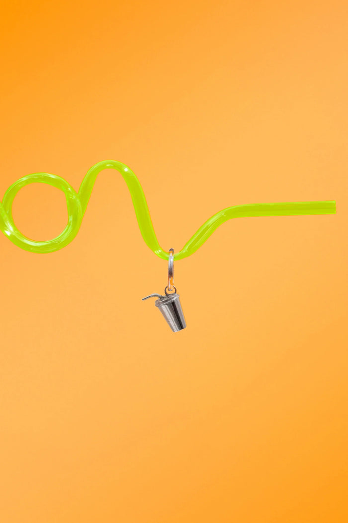 Green curly straw against a bright orange background, with a silver hoop with a silver metal, 3D fountain drink can charm.