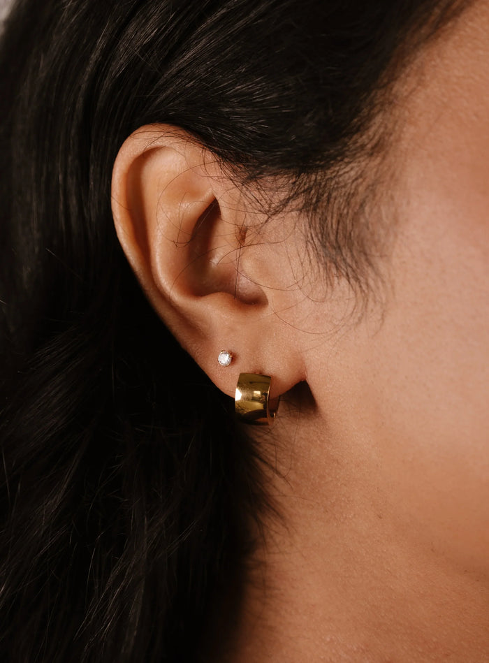Close-up of an ear wearing a gold earring with a dark background