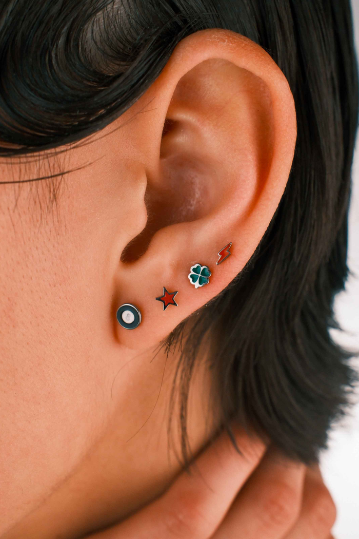 Photo of a person wearing multiple flat back stud earrings, including 1 in the shape of a star in cherry red enamel