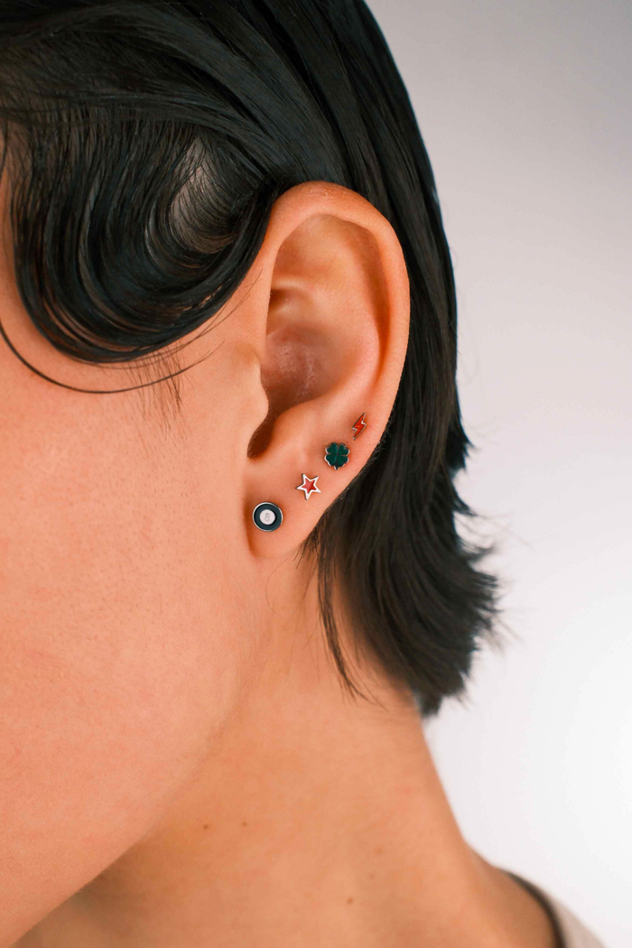 Photo of a person wearing multiple flat back stud earrings, including 1 in the shape of a star in cherry red enamel