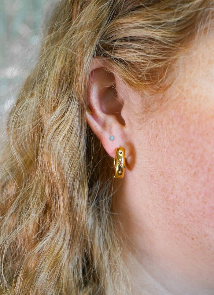 Close-up of a person wearing a gold hoop earring with a blurred background
