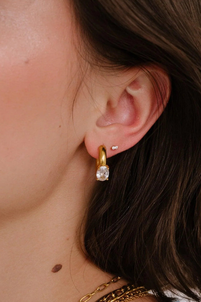 Close-up of a person wearing gold necklaces and earrings with a neutral background