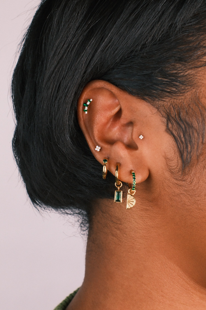 Close-up of an ear with multiple earrings on a plain background