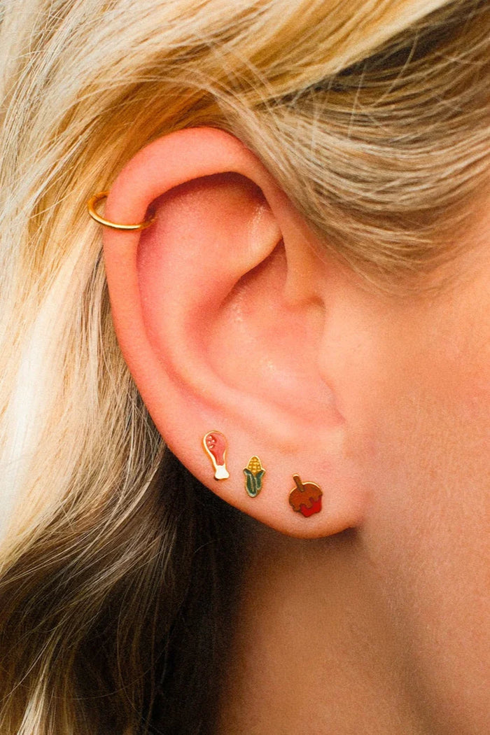 Close-up of an ear with gold hoop earrings and colorful studs.