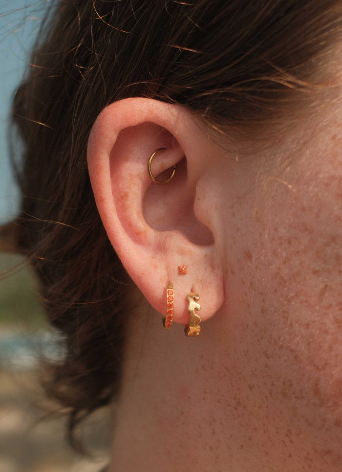 Close-up of an ear with gold hoop and stud earrings against a blurred background