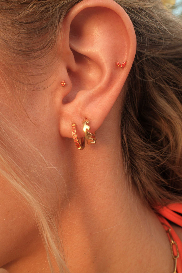 Close-up of an ear wearing gold hoop earrings with a blurred background
