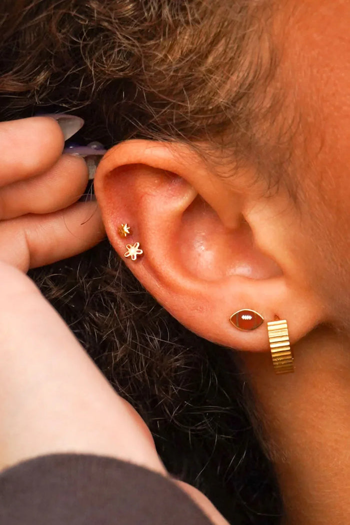 Close-up of an ear with gold earrings against a blurred background