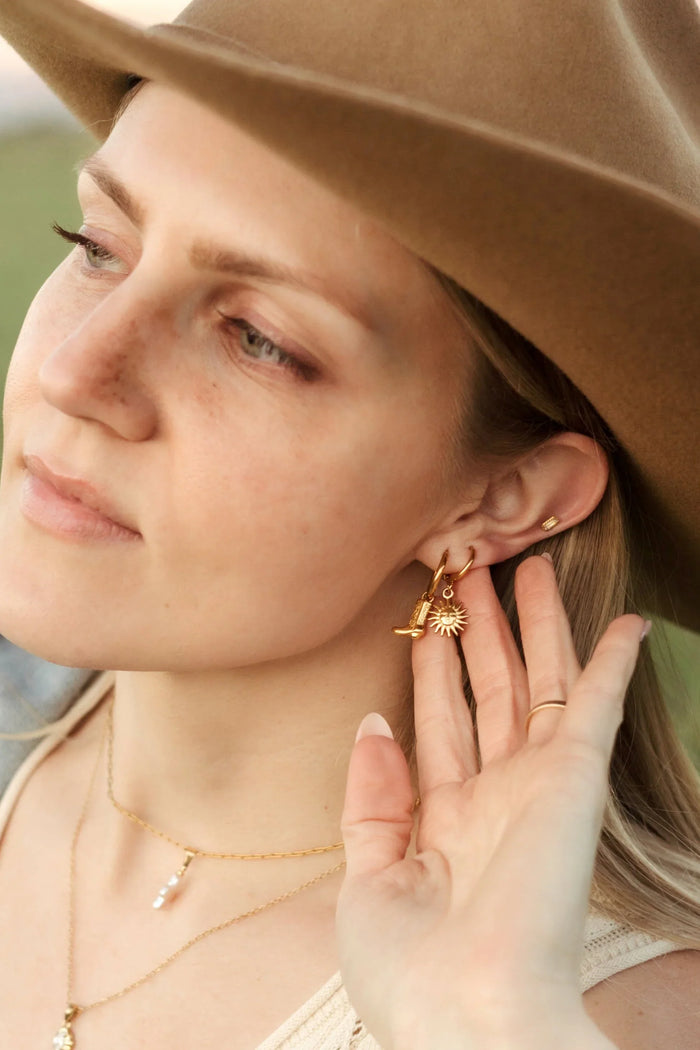 Woman wearing a brown hat and gold jewelry, including earrings and a necklace.